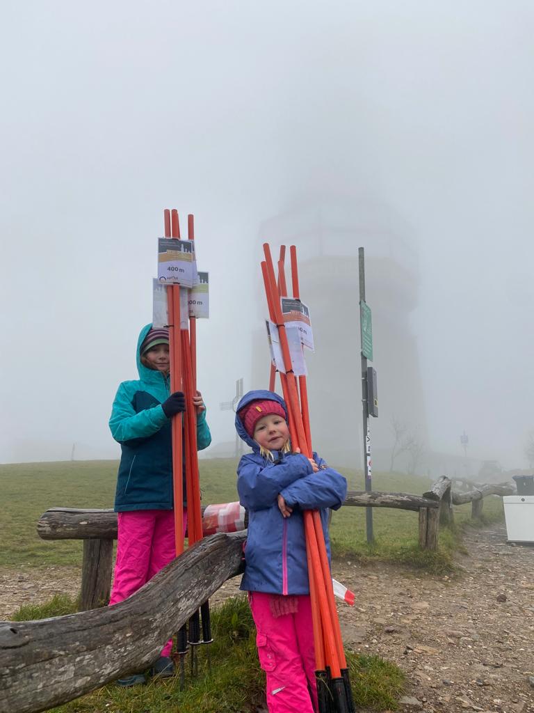 zwei fleißige junge Helferinnen präsentieren vor dem Feldbergturm im Nebel die abgeräumten Wegzeichen.